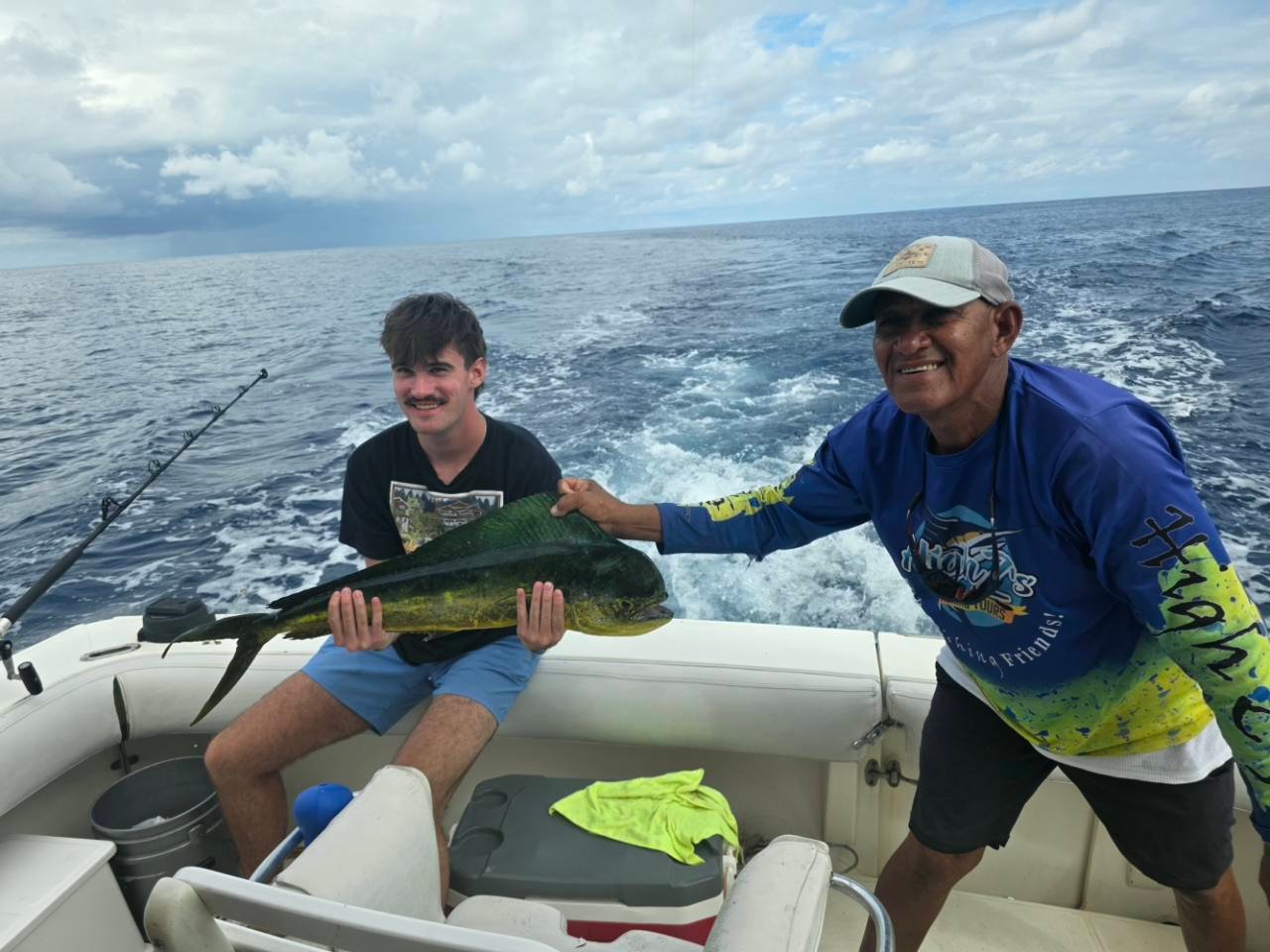 A High Z's crew member and a guest hold a large mahi while the boat is underway