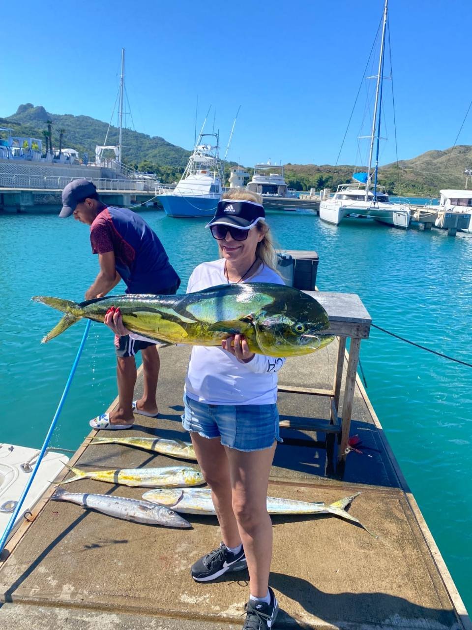 A guest holds a large mahi beside the turquoise water at the marina